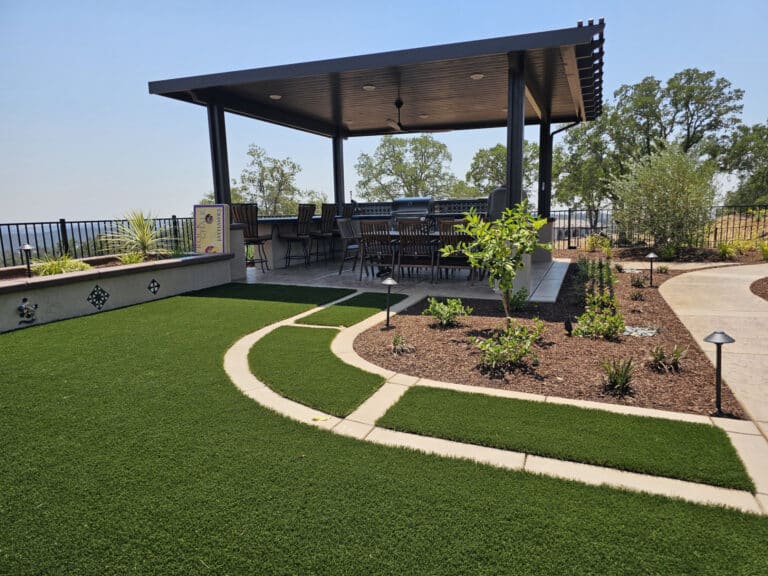 Custom outdoor living space in El Dorado Hills with a covered outdoor kitchen, seating area, artificial turf, and lush landscaping