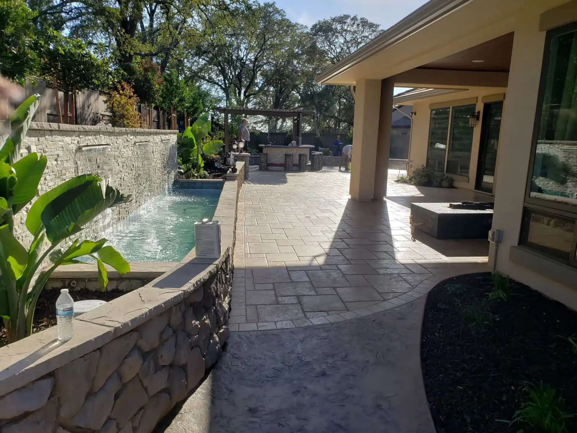 Stamped concrete patio with a stone waterfall pool and outdoor kitchen area.