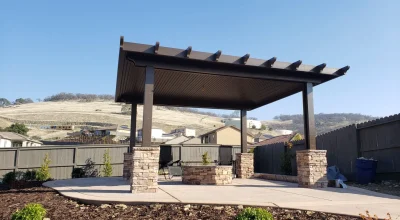 Backyard patio with brown pergola, stone fire pit, and new landscaping.