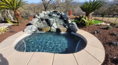 Outdoor spa with rock waterfall, palm trees, and lush landscaping.